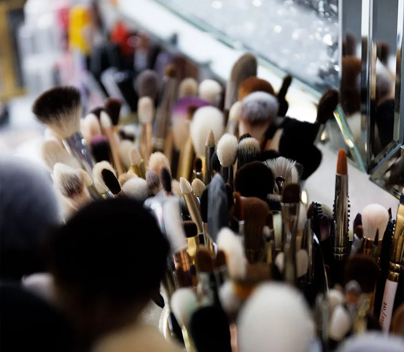 Eine Vielzahl von Schminkpinseln und kosmetischen Werkzeugen, die im Workshop verwendet werden, sind in Behältern auf einer Theke in der Region Aachen versammelt, die sich in einem Spiegel im Hintergrund spiegelt.